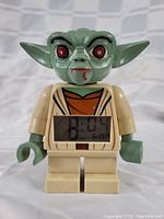 Front view of the Yoda LEGO alarm clock showing digital time 8:04 with the alarm set at 6:00, and Yoda's detailed face with red eyes and black eyebrows.