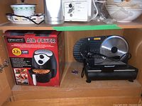 Photo of Techwood food slicer and boxed Gravitti air fryer in wooden cabinet storage