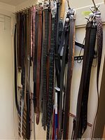 Belts hanging on white rack with various colors and materials including brown, black, and leopard print
