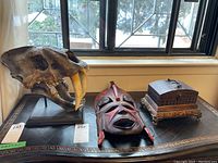Photo showing the three main items: faux skull, mask, and decorative wood box on a table by a window.