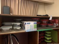 Wide view of two shelves filled with various glass food storage containers including boxed Glasslock set and Anchor containers with red and green lids.