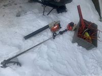 Overview of all tools on snow: Stihl blower, Echo string trimmer, Ryobi hedge trimmer blade and extension cords in crate