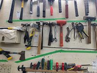 Overview of multiple hand tools hanging on wall, including hammers, mallet, wrenches, clamp, screwdrivers, and hatchets.