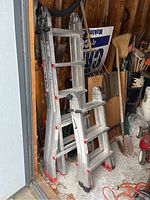 Two folded aluminum ladders with hinge lock joints stored upright in a shed among tools