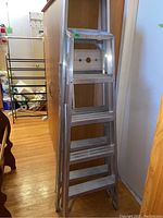 Photo showing two aluminum step ladders leaned upright; visible wide steps and side braces.