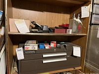 Top shelf showing heavy-duty hole punch, red plastic paper trays, stainless steel pump dispensers