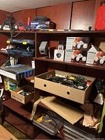 Photo of shelving filled with assorted tools, Noma security lights in boxes, boxed and loose tools, electrical wires, automotive parts, and equipment.