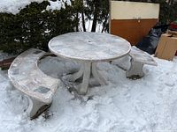 Full photo of round stone table with mosaic tile top and three semicircular benches in snow.