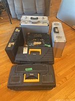 Overview photo showing all seven cases including briefcase, toolboxes, aluminum cases, and vintage metal box arranged on floor.