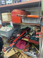 Shelf with red and cream metal toolboxes, electric chainsaw, pole saw, hand saws, and assorted small tools and hardware.