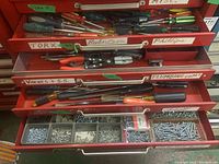 Four metal drawers filled with various hand tools and small hardware inventory including screwdrivers, plumbing tools, and compartments of screws and bolts.