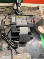 Front view of WEN wet wheel sharpener showing power cord wrapped and placed to the left side with cordless phone in background.