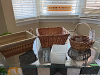 Four baskets displayed on glass table near window; includes rectangular lined basket, medium rectangular basket, small round basket, and a small white square container.
