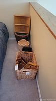 Photo showing four items: two wicker baskets, a rectangular basket with wood hangers, and a white ceramic crock on carpet next to a bed.