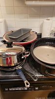 Wide view of pots and pans on kitchen counter including enamelware roaster, wok, stainless steel pot with lid, and baking pans.