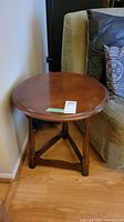 Front angled view of round wooden end table next to sofa, showing top surface with hole and wooden finish.