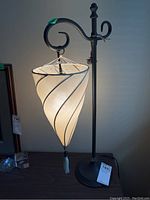 Full view of the desk lamp showing the metal base, stand with curled arm, and hanging swirl-patterned lampshade with tassel.