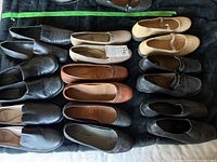 Top view showing 10 pairs of women's shoes in black, brown, tan, and beige lying side by side on a dark surface.