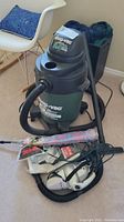 5 gallon Shop-Vac with hose, some vacuum attachments, and Shark vacuum on carpet near white chair.