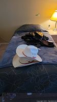 Photo showing single bed made with bedspread and bedding, with items like hats and shoes on top. Lamp and bedside table visible.