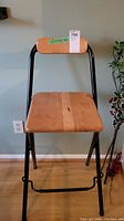 Front view of folding stool showing wooden seat, backrest, and black metal frame.