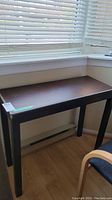 Photo of the wood table placed beside window showing leather-like top and stitchwork detail.
