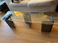 Side view showing the glass top and stone bases of the coffee table placed before a couch on a wood floor.