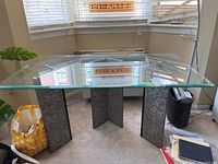 Full view of the rectangular glass top table with stone base in a room showing its size and structure.