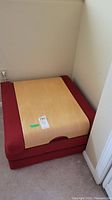 Photo of red folding foam bed folded up with wooden table surface attached on top.