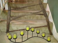 Antique wooden buck saw leaning on carpeted stairs with metal candelabra holding seven glass votives with yellow candles in front.