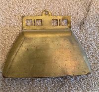 Brass crumb catcher showing tarnish and rectangular cut-out handle detail.