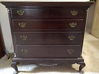 Front view of antique mahogany dresser showing four drawers with brass handles, scalloped apron, and cabriole legs.