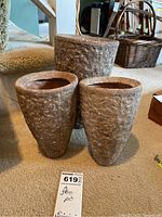 Three textured, clay-like flower pots arranged on carpet, showing the full set and size variations.