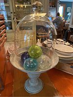 Glass cloche on tin stand holding five crackled glass balls in green, blue, and clear colors.