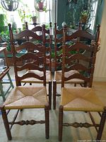 Photo showing four wooden rustic farmhouse ladder back chairs with woven seats, one chair has cracked spindle, one has frayed seat weave. Chairs show scratches and wear.