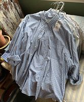 Photo showing a collection of men's XXL long sleeve dress shirts, mostly blue plaid with button-down collars, hung on a hanger.