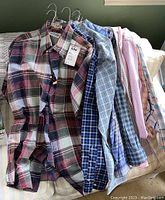 Photo showing several men's XXL long sleeve button-down dress shirts, hung on hangers, displaying variety in color and pattern including red, green, blue, and pink checks and plaids.