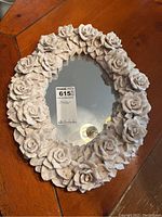 Full view of the floral oval mirror on a wooden surface, showing the overall shape and frame decoration composed of resin roses and leaves.