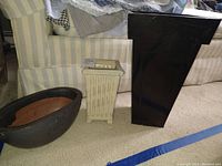 Three plant vases displayed on floor next to striped chair; includes brown-black oval ceramic vase, off-white square ceramic vase, and tall black metal vase.