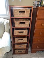 Front view of the tall wooden shelving unit with six wicker baskets inside compartments.
