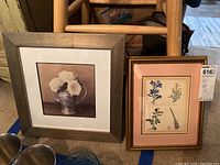 Photo showing two framed prints side by side; one with white roses in a silver cup and the other with botanical flower illustrations, the former in a rustic wood frame and the latter in a gold decorative frame.