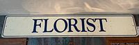 Full view of vintage Florist sign showing 'FLORIST' in large blue letters on white metal background with blue border.