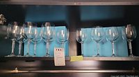 Seven red wine glasses and four white wine glasses on shelf with tags and markings visible