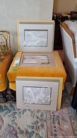 Three white embossed or 3D textured prints stacked on a yellow stool, matted and signed by Calvin Nichols.