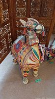 Front and side angle showing colorful fabric patterns, tassels, and bead adornments on camel figurine.