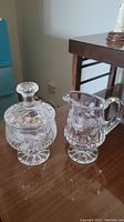 Photo of two crystal pieces: pedestal sugar bowl with lid and pedestal creamer, both with etched cornflower patterns.