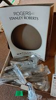 Open box with Rogers Stanley Roberts branding showing stainless steel cutlery wrapped in plastic and bundled inside.