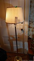 60-inch floor lamp with pleated cream fabric shade, brass-tone base and pole, shown standing in front of a door.