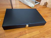 Closed black flatware storage case with gold-tone clasp on hardwood floor.