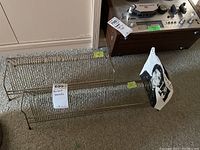 Two metal wire record stands on carpeted floor near a vintage audio component.
